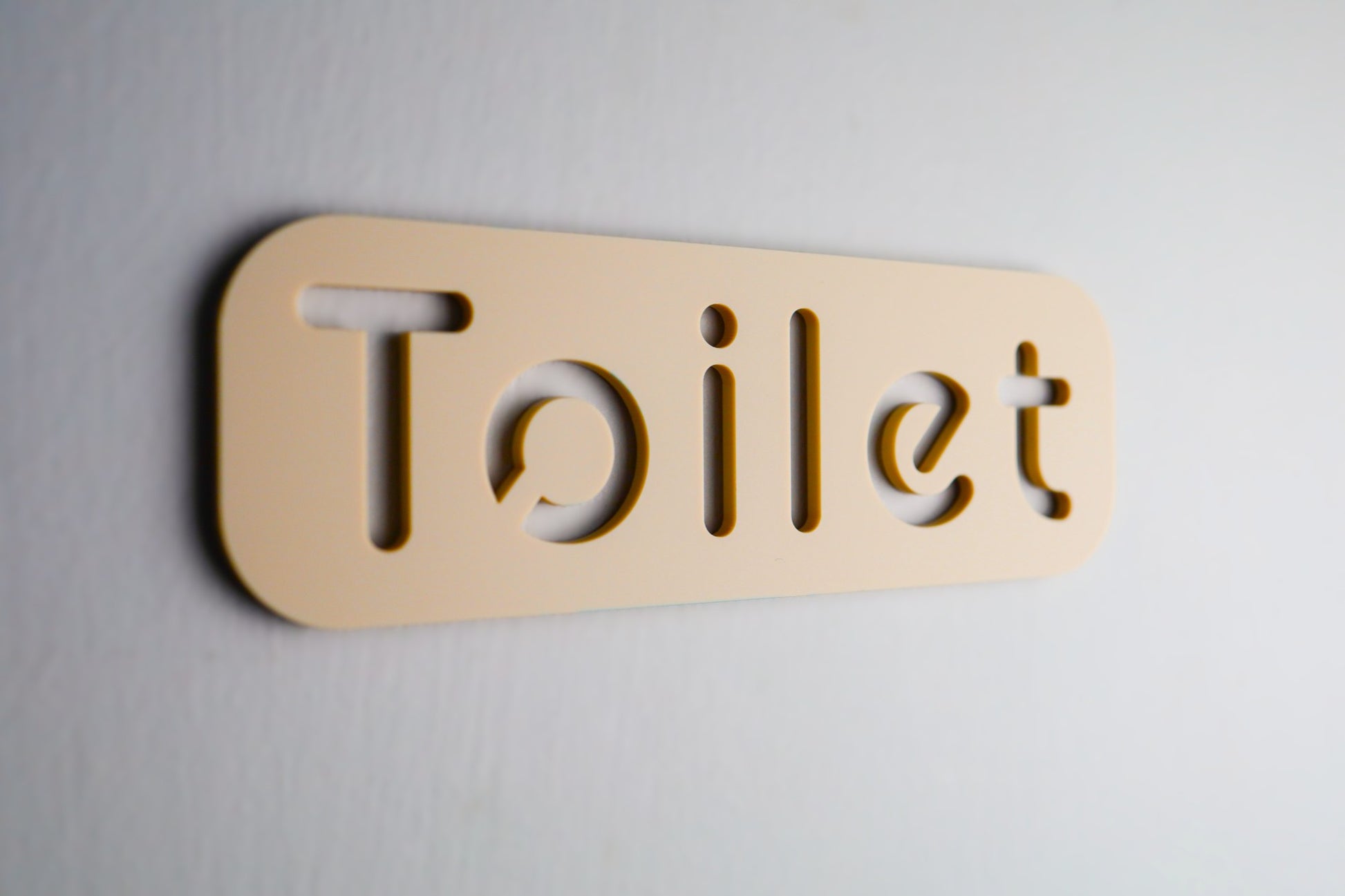 Beige acrylic WC sign with clean, legible typography installed on a wall.