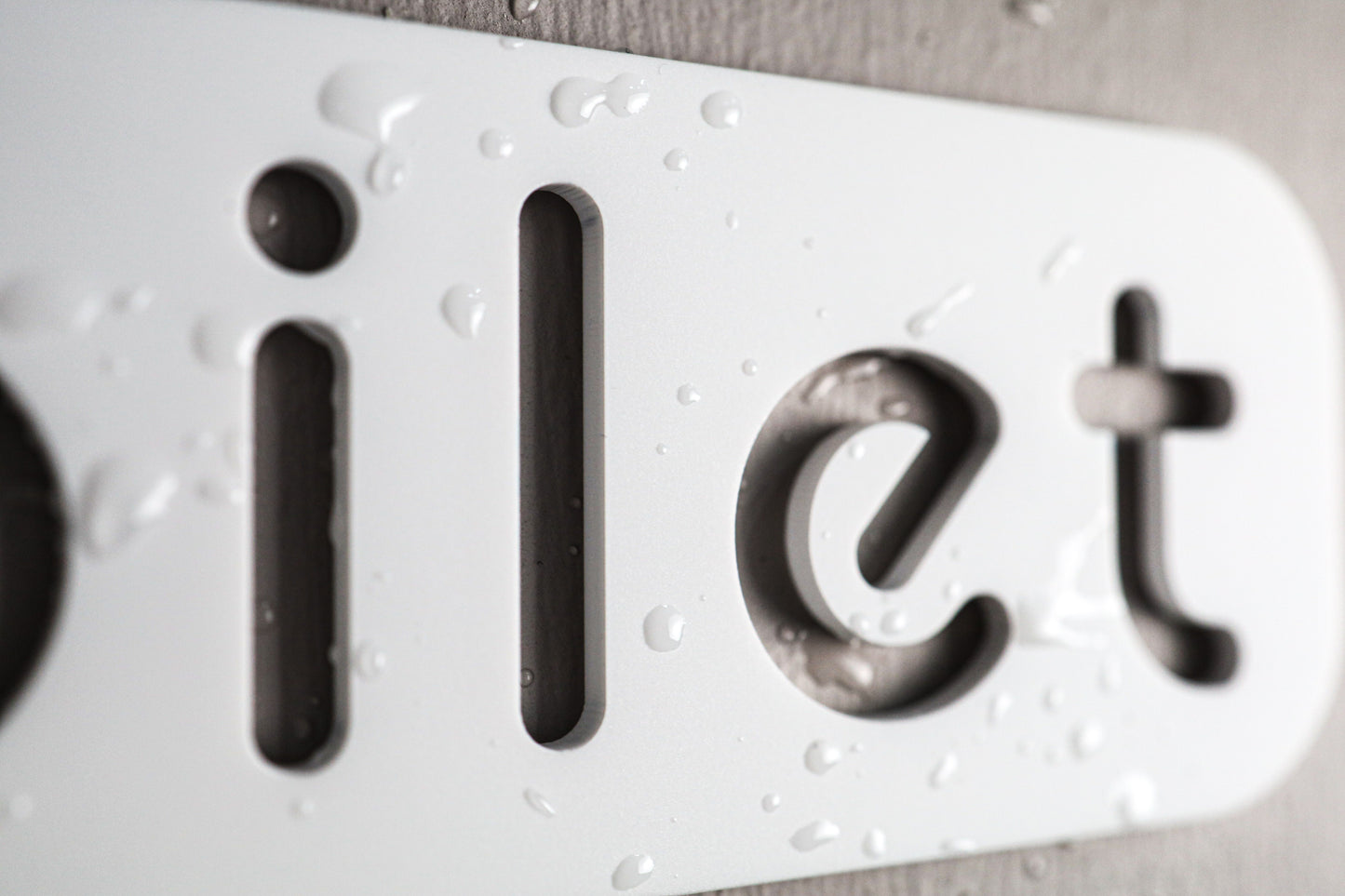 Cut-out lettering toilet sign with a refined stone texture on white acrylic.